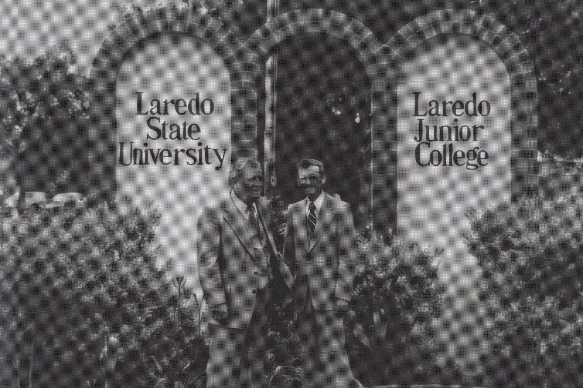 Two men standing in front of a mural that reads 'Laredo State College' and 'Laredo Junior College'.