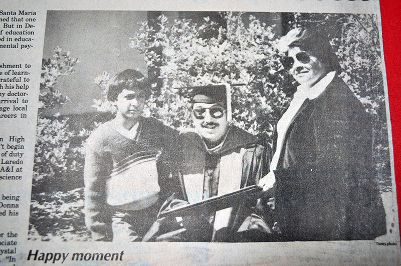 Julio F. Madrigal smiles with his diploma. To his left is his adolescent son and standing to this right is his wife.