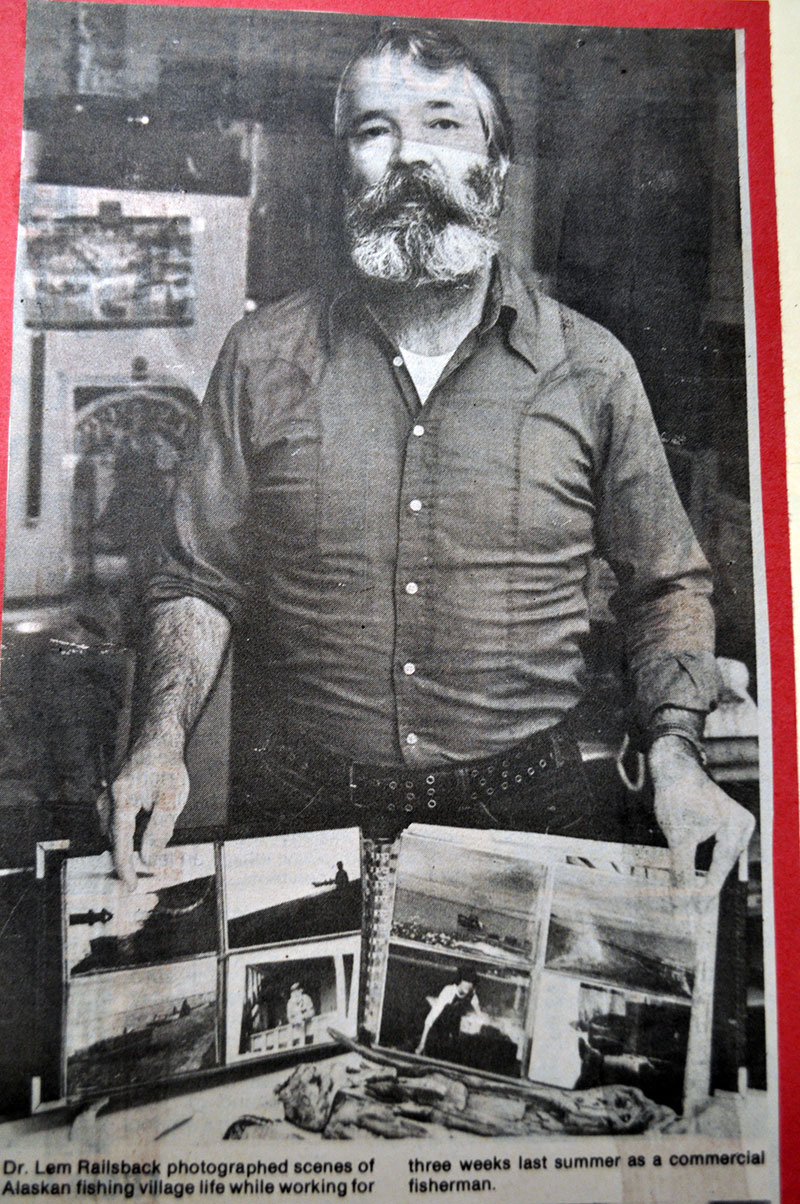 Dr. Railsback holding a scrapbook filled with photographed scenes of an Alaskan fishing village.