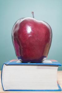 Stock image of a red apple sitting atop a large book.