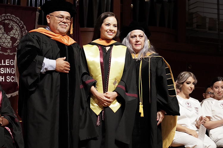 Graduate standing between two professors, receiving her Nursing hood at the Nursing Hooding and Pinning ceremony