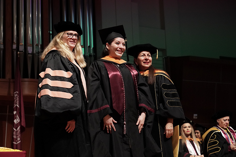 Graduate standing between two professors, being hooded during the Nursing Hooding and Pinning ceremony