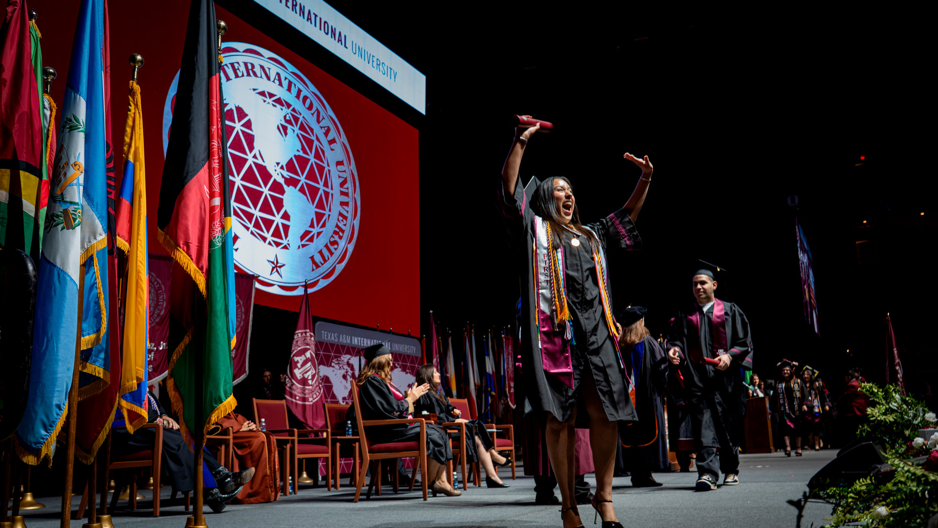 A spring 2026 graduate crosses the stage and lifts her hands in the air.