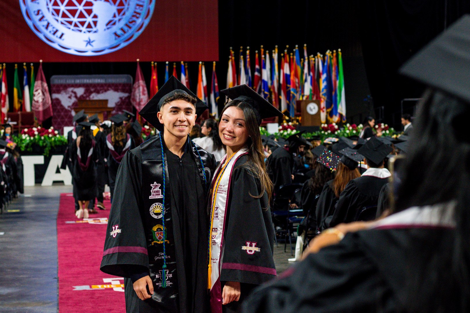 Two grads stand together and pose for a photo while smiling.