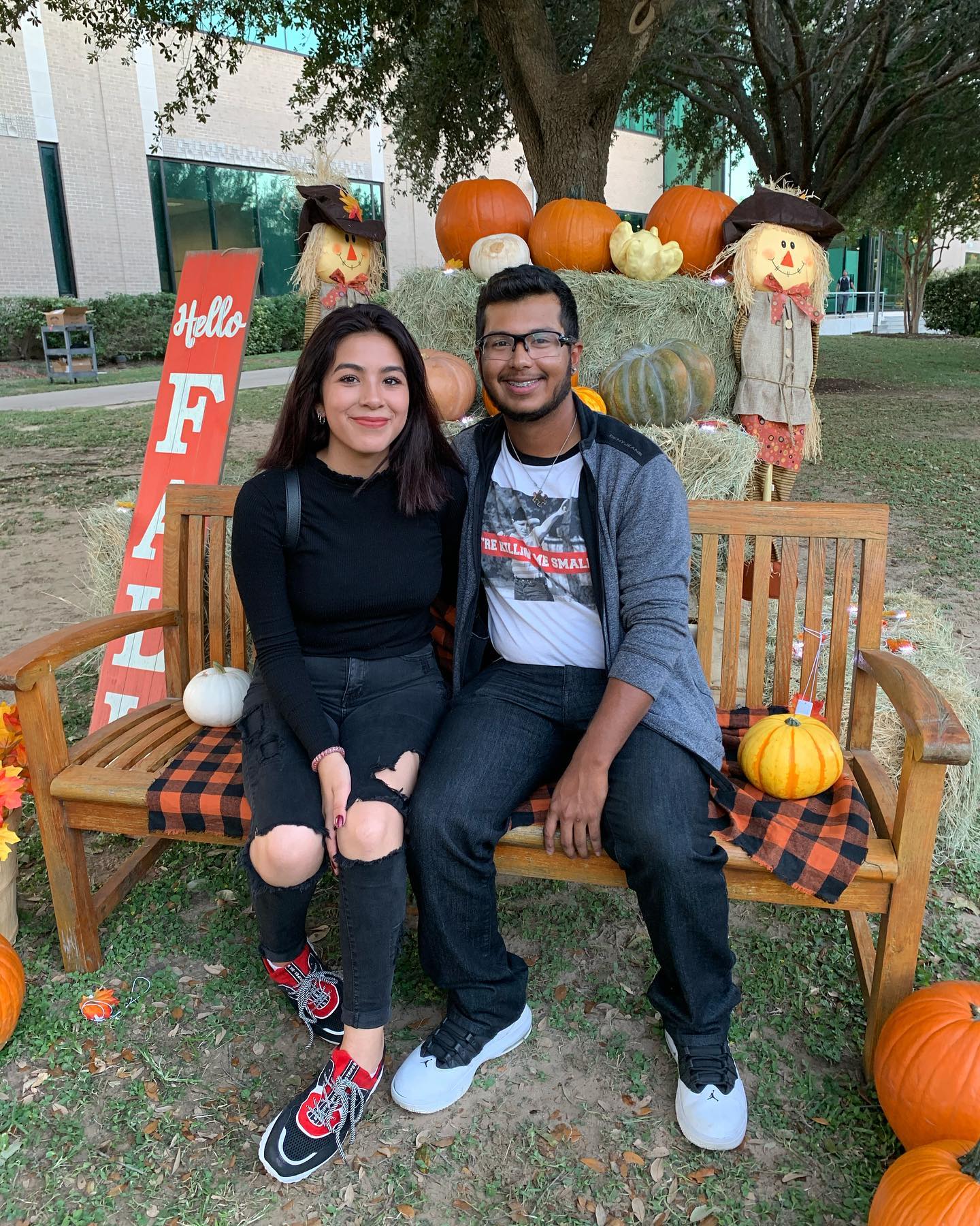 Female and male student posing on a bench in front of a pumpkin patch