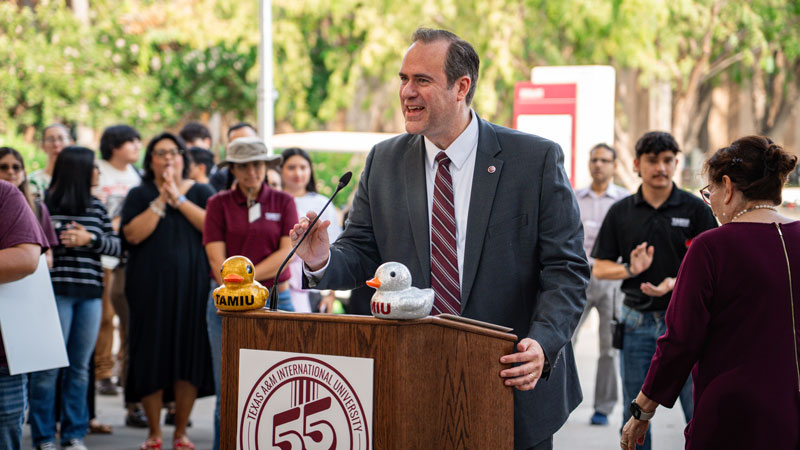 Dr. Maynard at podium with 55th Anniversary logo and two rubber ducks during Milestone event