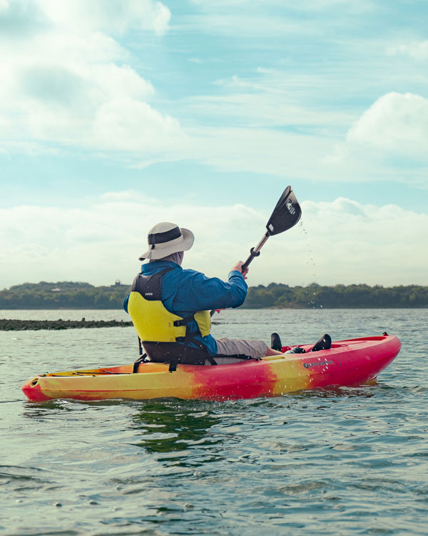 Kayaker in bright gear powers through open water under a vivid sky