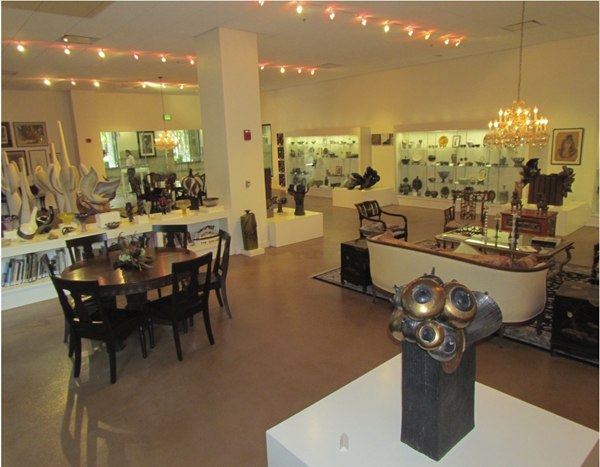 Portion of Helen Richter Watson Gallery replicating her studio. Pictured are two tables with various sculptures and art pieces surrounding them.