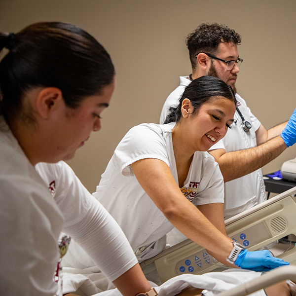 three nursing students working together to care for a mannequin in a simulation room. 