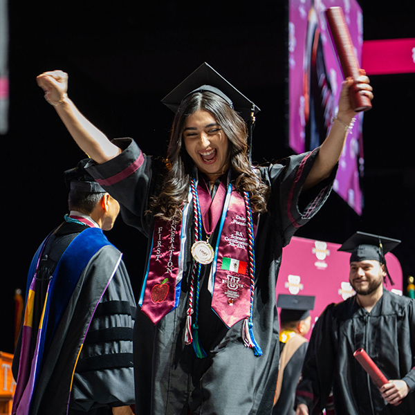 Graduate raises hands in the air as they cross the stage